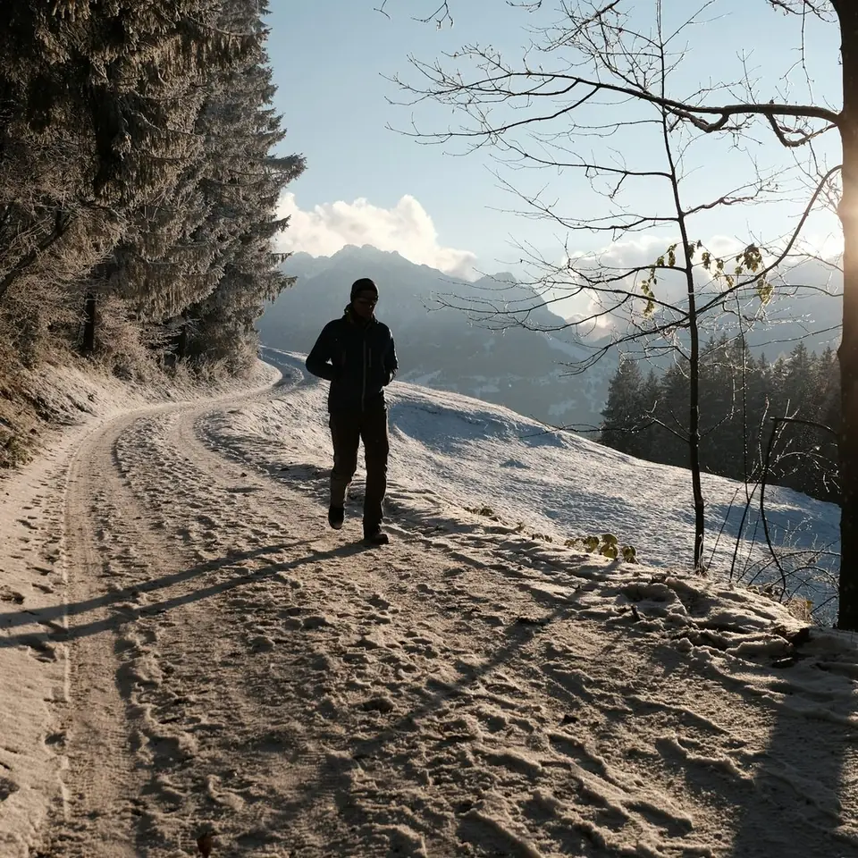 Runner in a black shell jacket on a snowy mountain trail