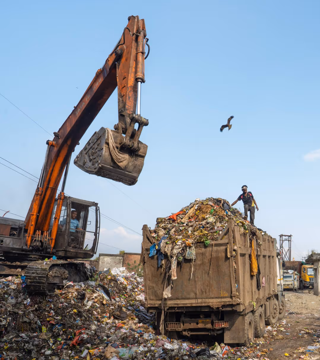 Excavator loading a truck filled with mixed waste at a landfill site