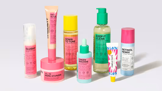 Seven colorful skincare products in tubes, bottles, and jars arranged in a row on a light surface, including items labeled Slushy, Face Glaze, Down to Tone, Green Machine, Keep It Clean, Pink Paste, and Retinol Remix.
