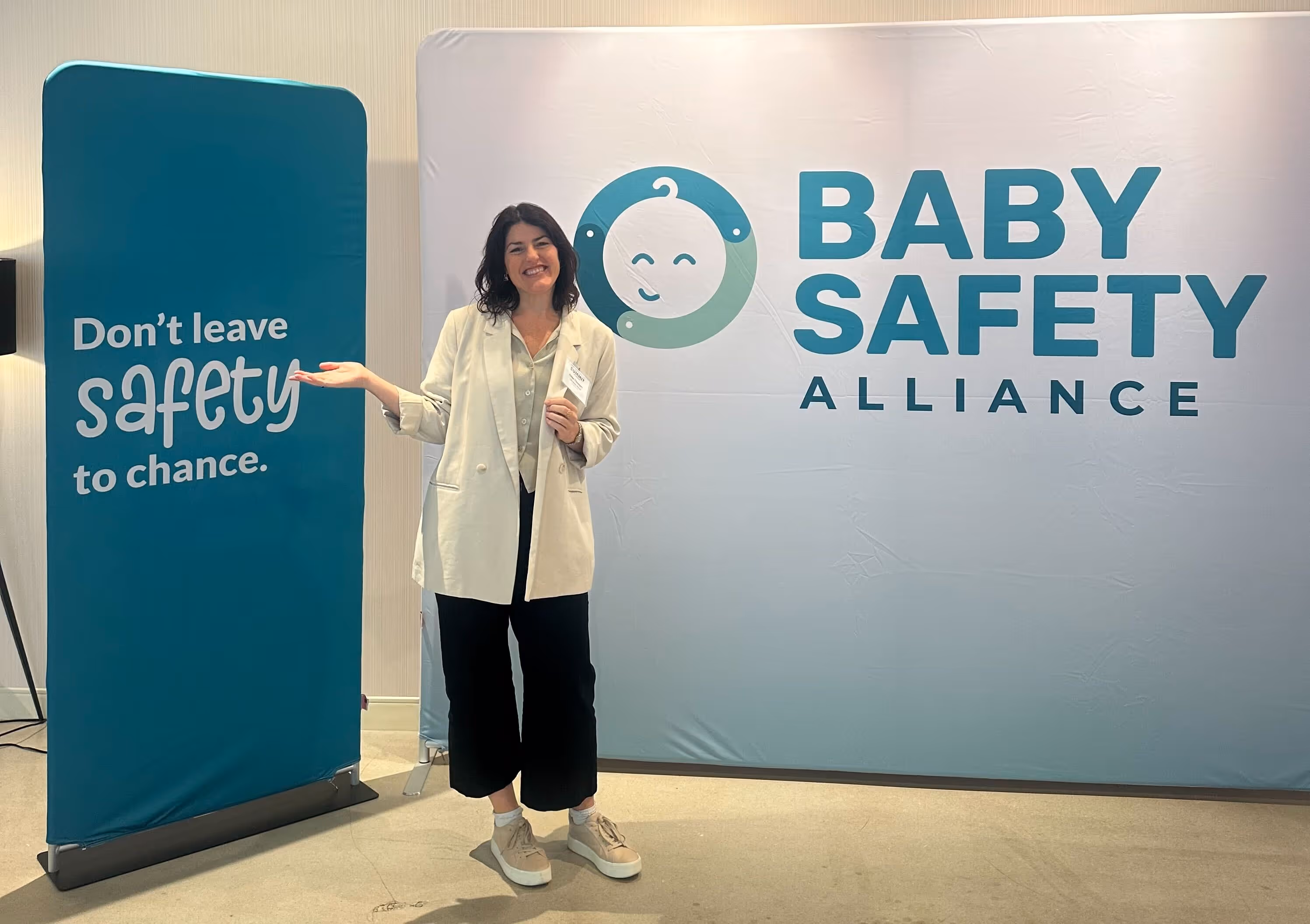 Woman smiling and gesturing at Baby Safety Alliance logo and banner stating safety should not be left to chance.
