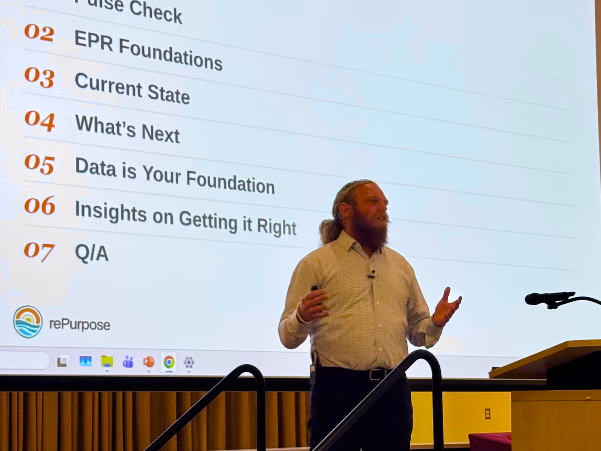 Man with beard giving a presentation next to a screen listing seven discussion topics for rePurpose.
