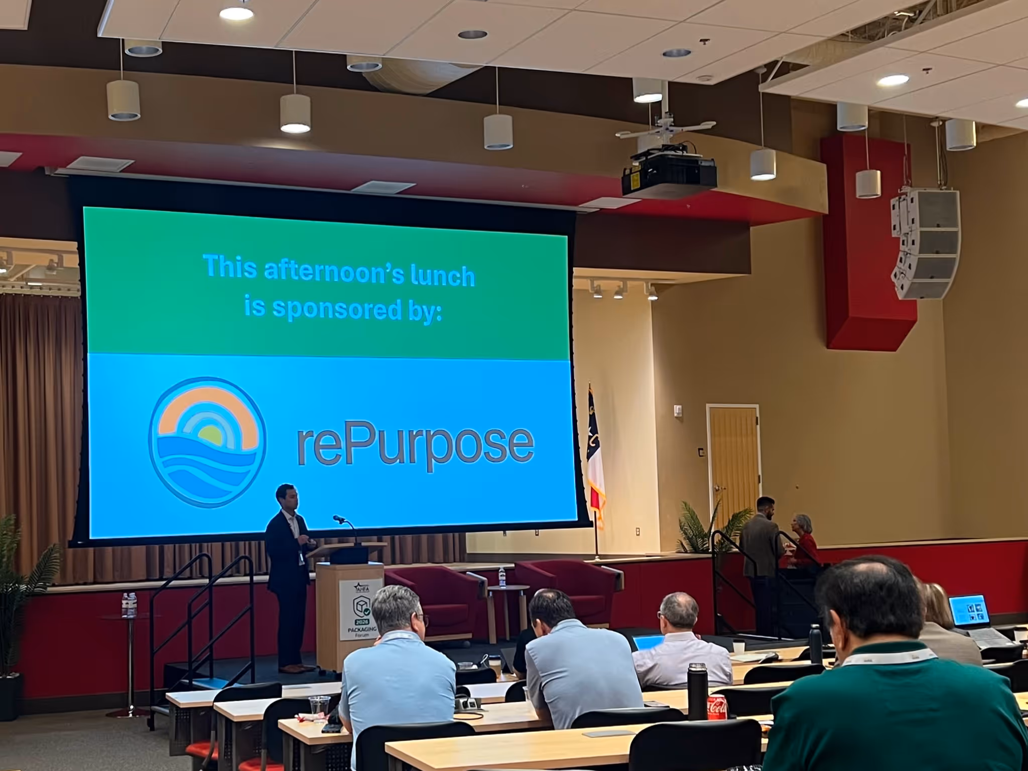 Conference room with attendees facing a screen showing ‘This afternoon’s lunch is sponsored by rePurpose.’