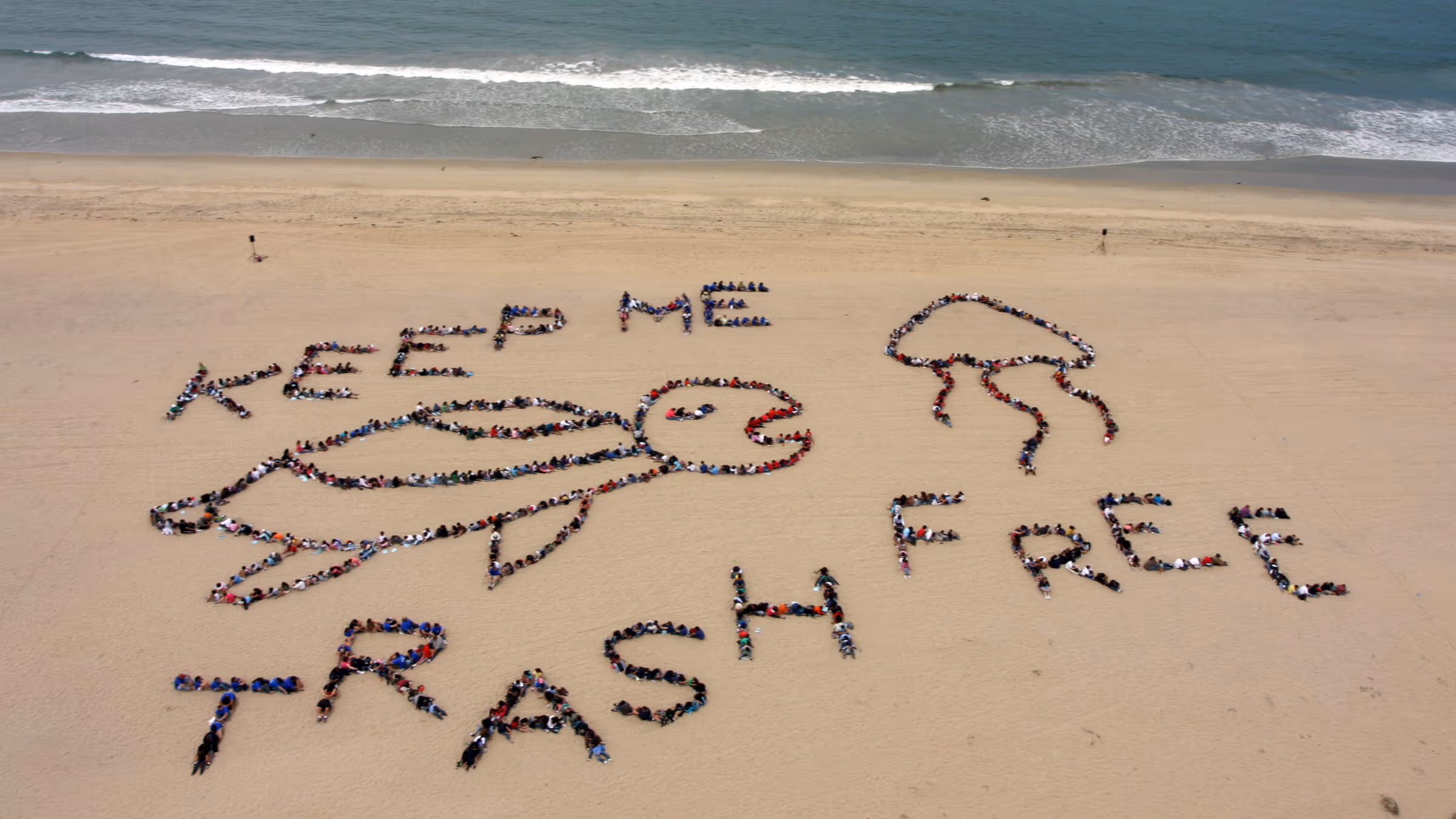 A group of students who spelled out "Keep Me Trash Free" with images of a turtle and a jellyfish with their bodies for an aerial shot on the beach
