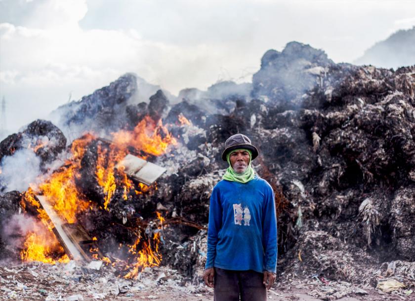 An Indonesian man standing in front of a pile of burning plastic causing air pollution