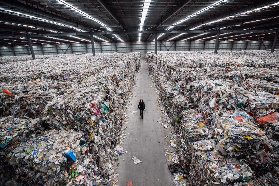 A person walking between piles of plastic stacked up