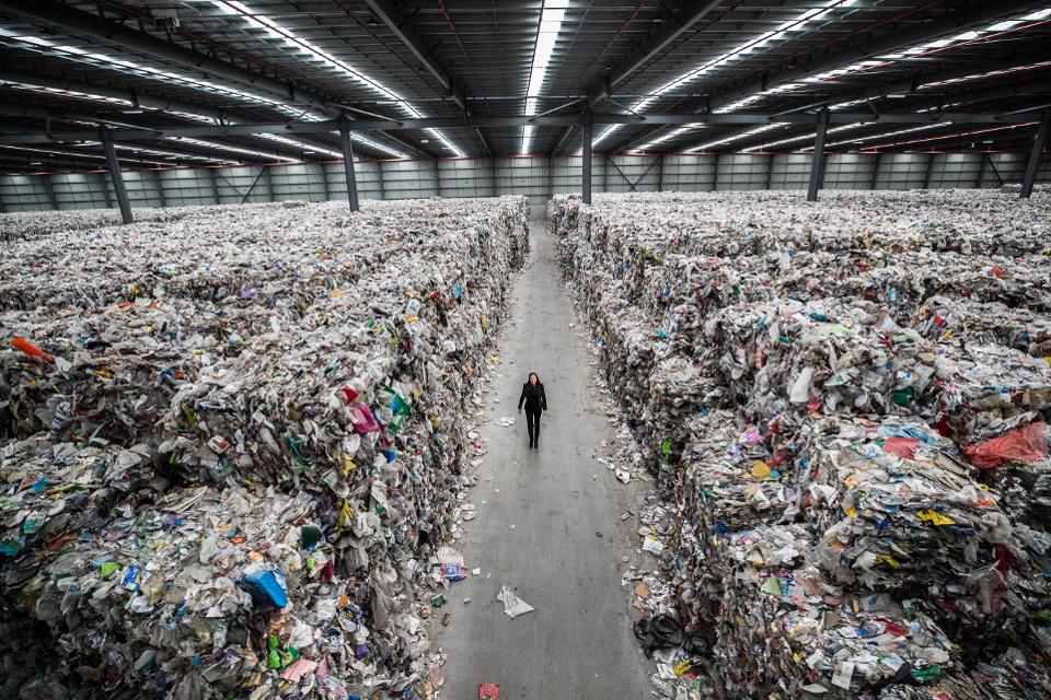 A person walking between piles of plastic stacked up