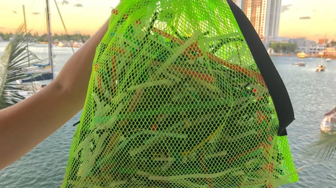 A person holding up a bag of straws and stirrers at a beach