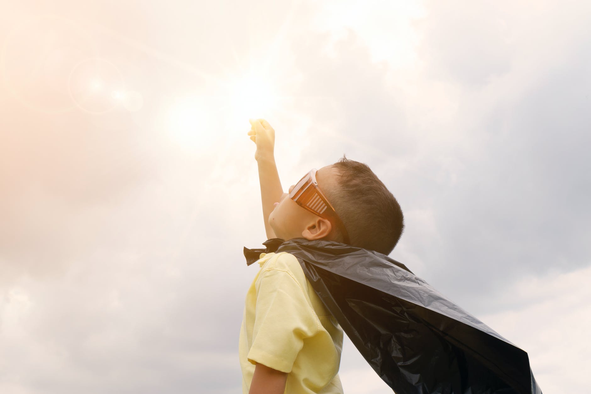 A boy pretending to be a superhero with a black plastic bag as his cape
