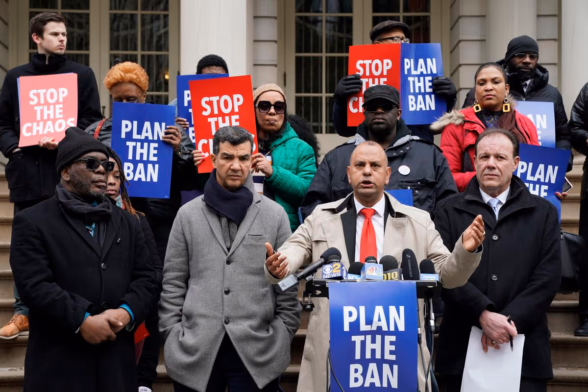 A group of people holding posters saying 'Plan The Ban' and 'Stop The Chaos' in New York