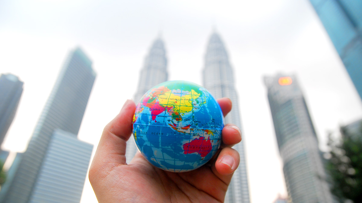 A hand with a globe in their palm in front of high-rise buildings