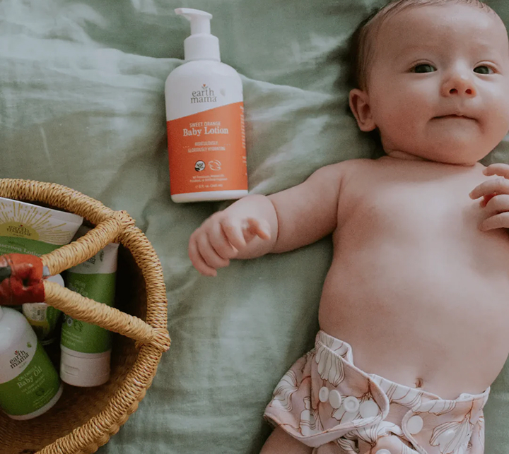 a baby lying on a blanket next to a basket of body lotions