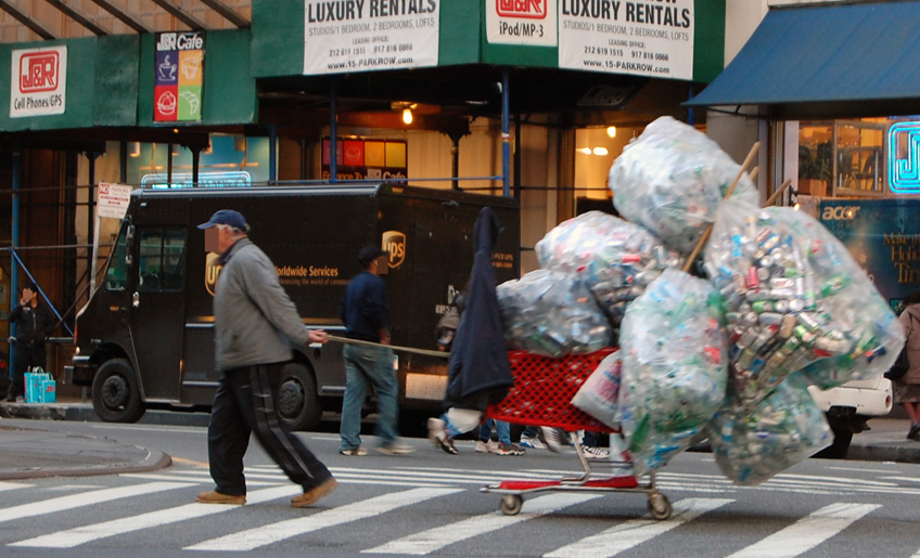 A man in NYC carrying a cart with huge plastic bags filled with plastic waste
