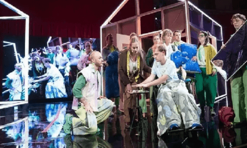 A group of actors gather around on stage in the middle of a performance.