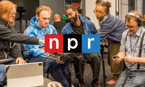 A group of five people sit together, looking at a laptop. NRP logo in the middle. “N” with red background. “P” with black background. “R” with blue background.
