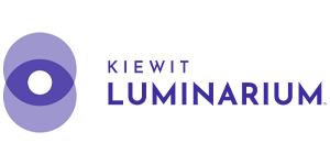 A logo in shades of gray, featuring an abstract circular design on the left that looks like an eye or lens, with overlapping shapes. To the right of this design, the text reads "KIEWIT LUMINARIUM" in uppercase letters, with "KIEWIT" in a smaller font above "LUMINARIUM," which is larger and bold.