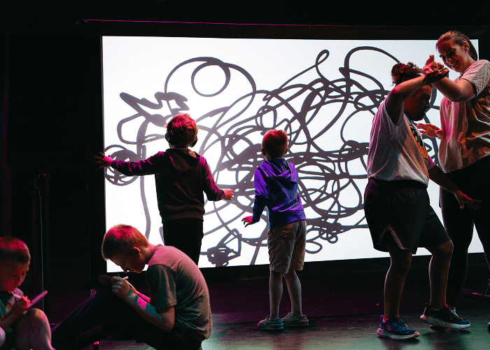 Two children looking at wall art. Two in front of them sitting down. Two other people to their right dancing.