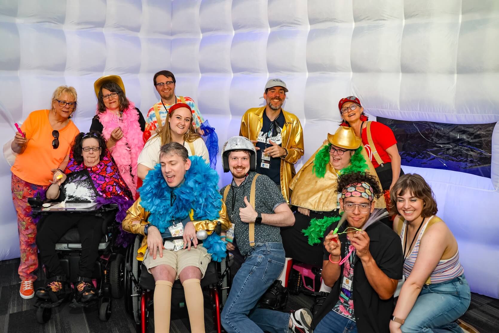 Twelve people gathered together in bright and fun clothing and accessories, smiling. Two of the attendees are in wheelchairs.