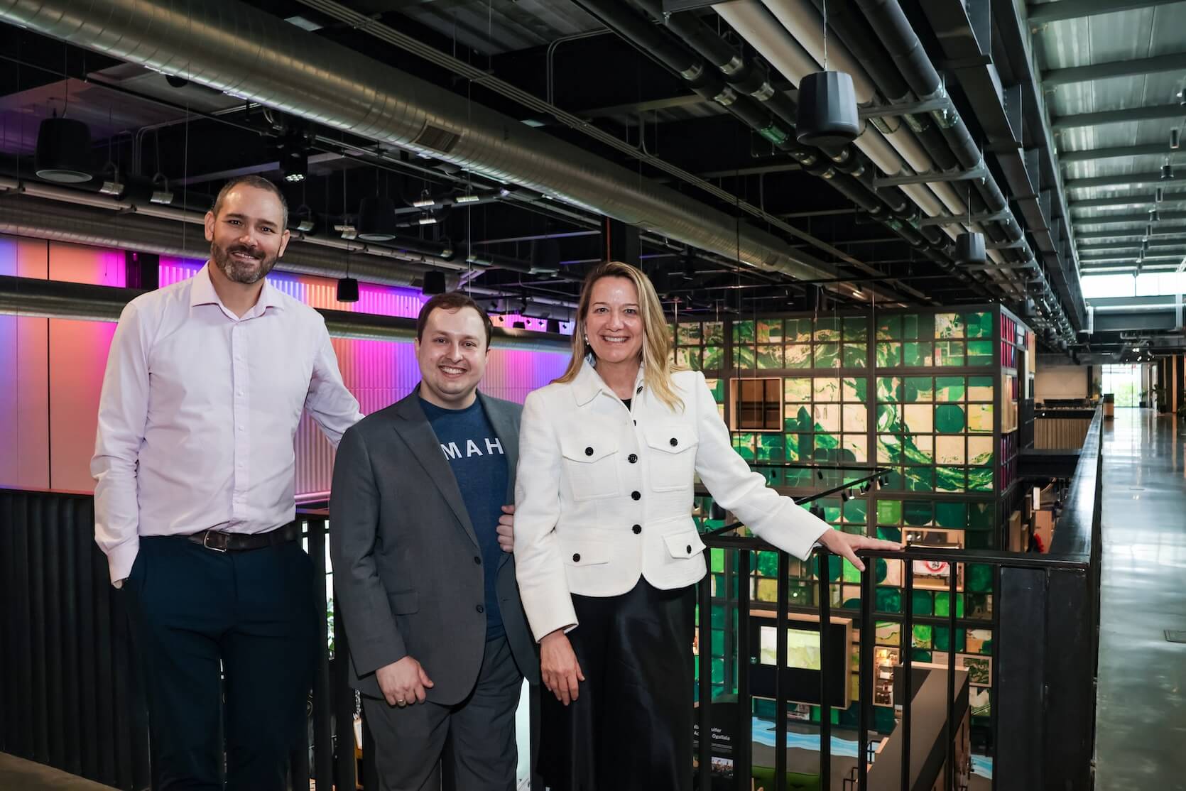 A tall man with short shaved hair and a beard, wearing a light purple button up shirt and denim jeans. A shorter man with short brown hair, a blue t-shirt that says “Omaha” in white letters, covered by a grey blazer and pants. The last woman has long blonde hair, and is wearing a white jacket and long black skirt.