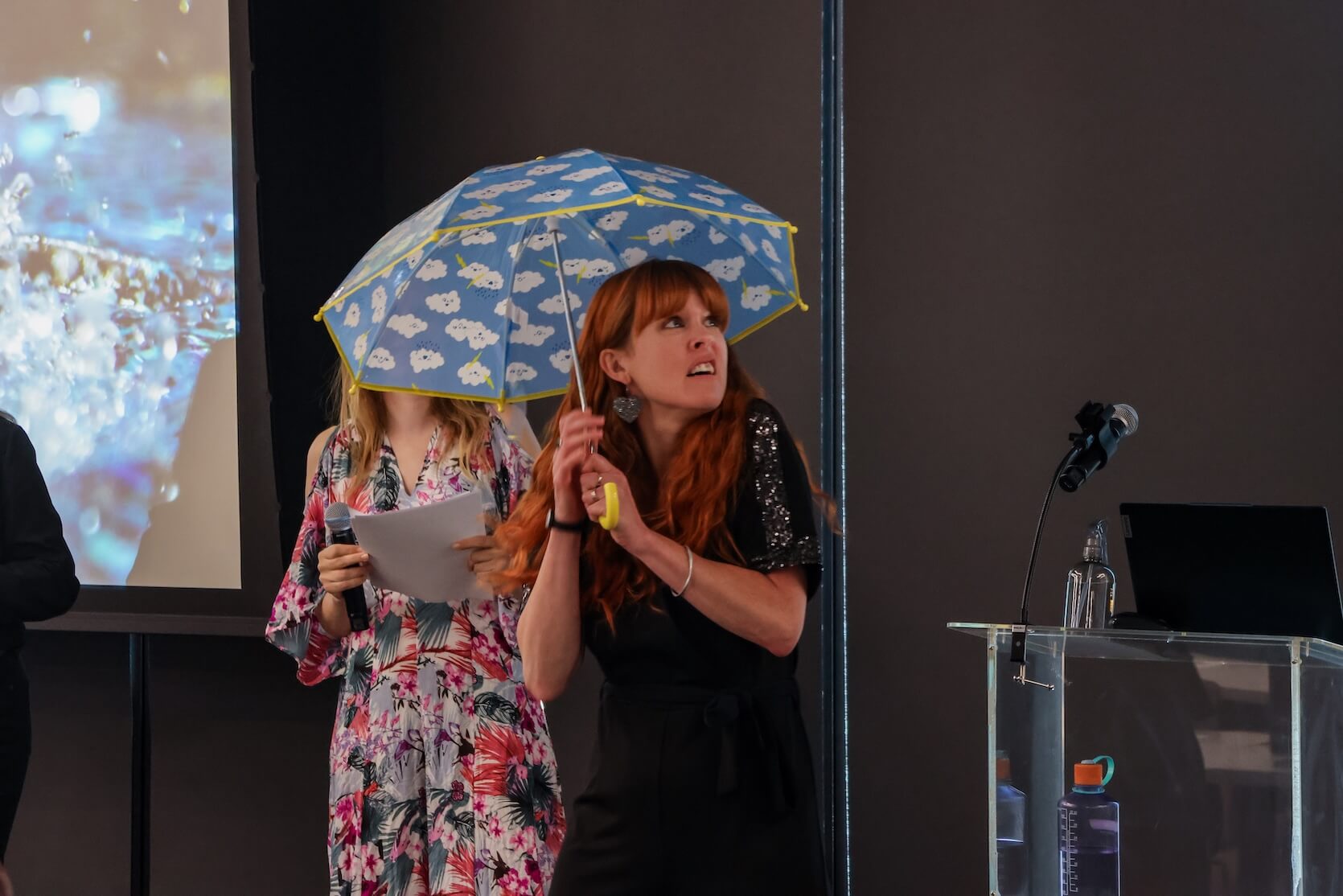 A white woman with long red hair with bangs, holding an umbrella, looks surprised/scared, looking away from the camera. This appears to be part of a demonstration of sorts.