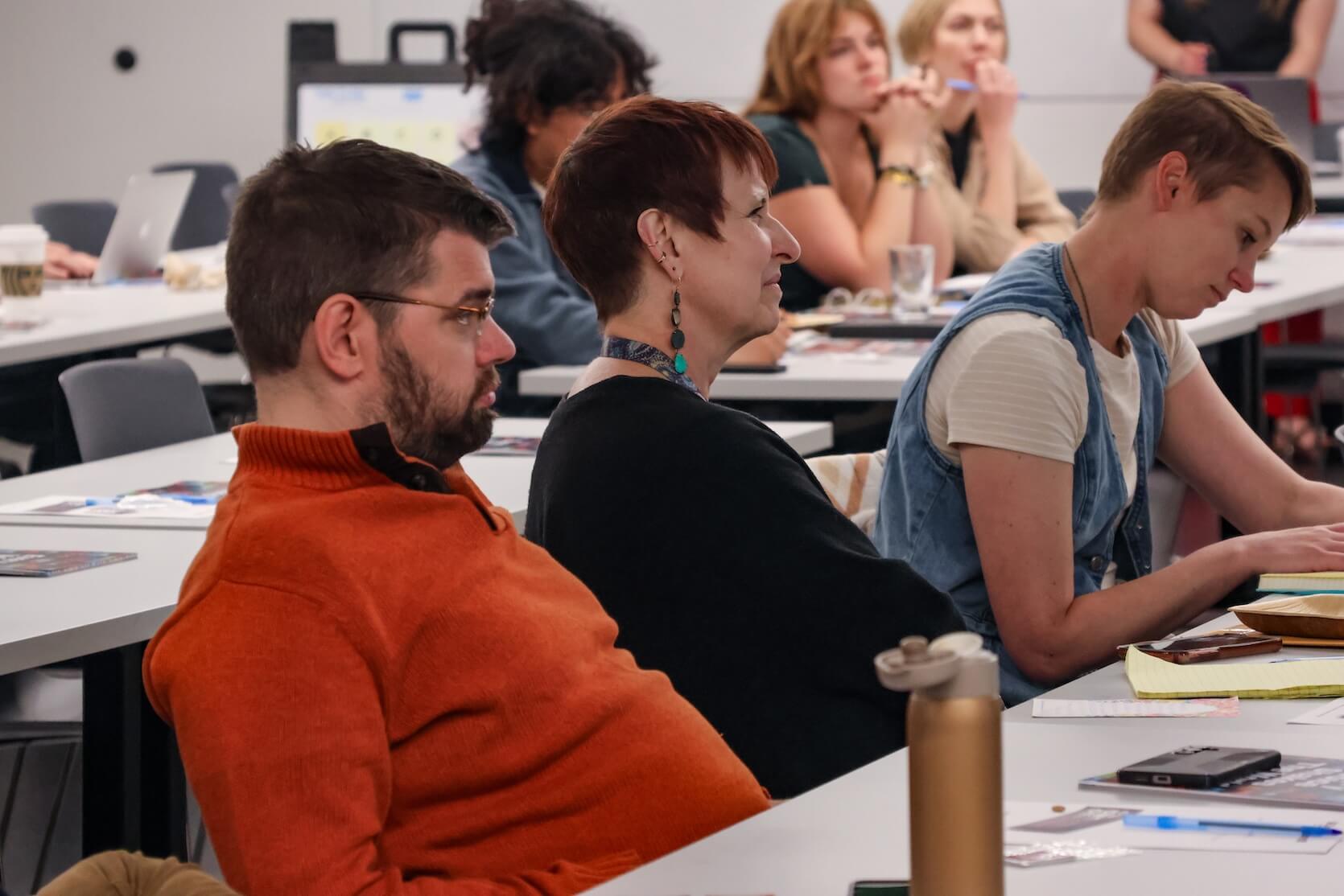 A white man and two white women sit at a table, focused on the speaker and material on the table.