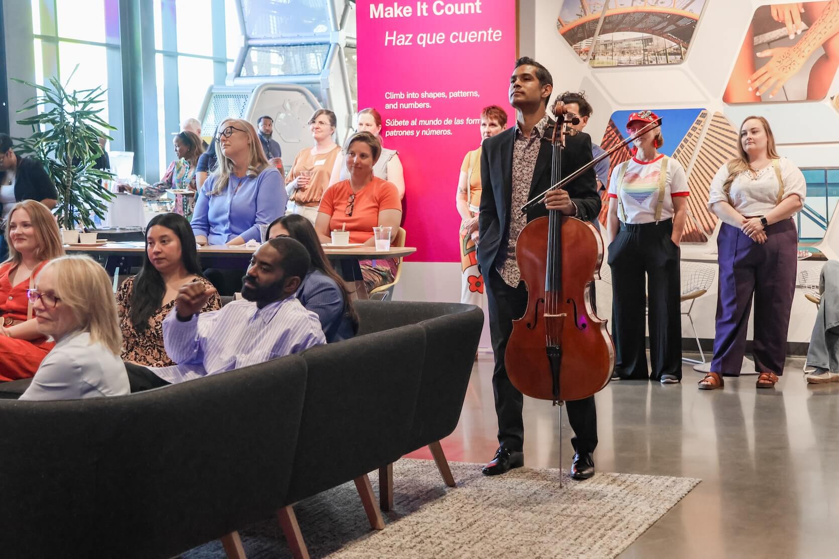 A large group of people are standing and sitting, focused on the speaker.