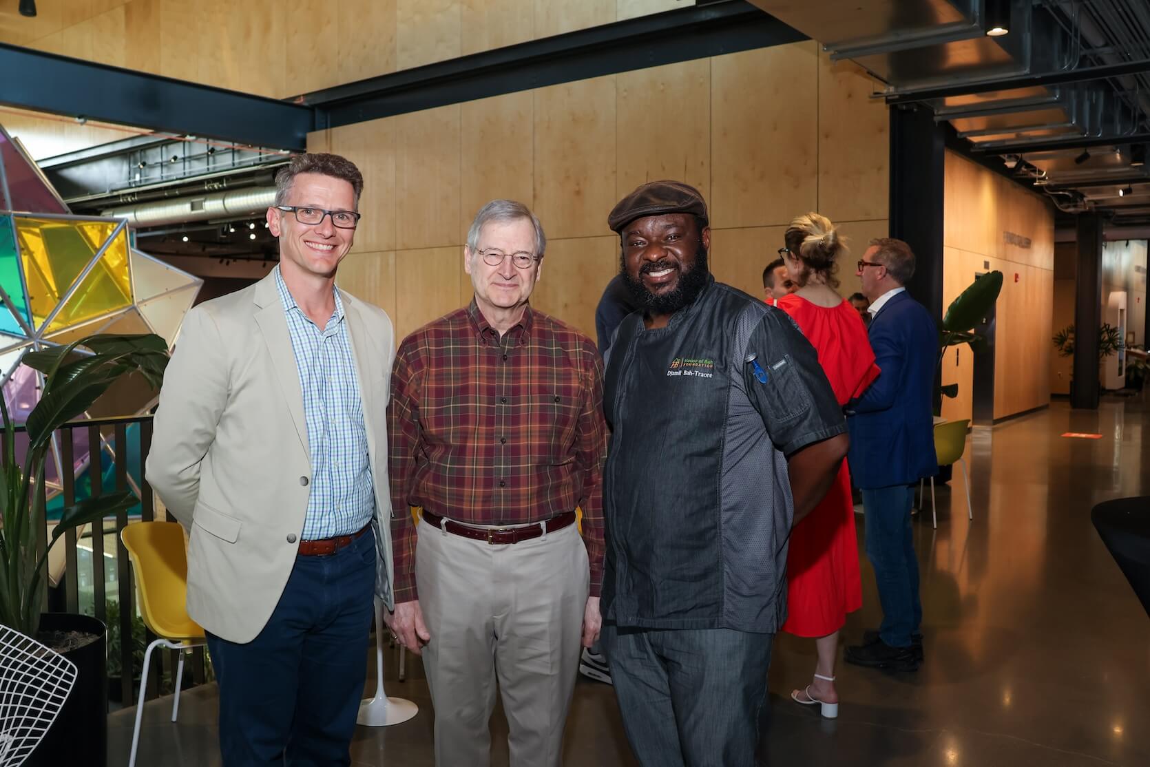 Two white men and one Black man stand together, smiling. They are in business casual attire.