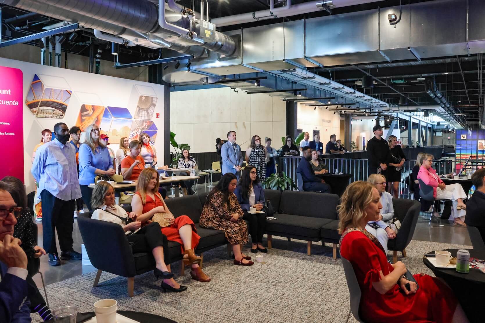 A large group of people sitting and standing, focusing on the speaker.
