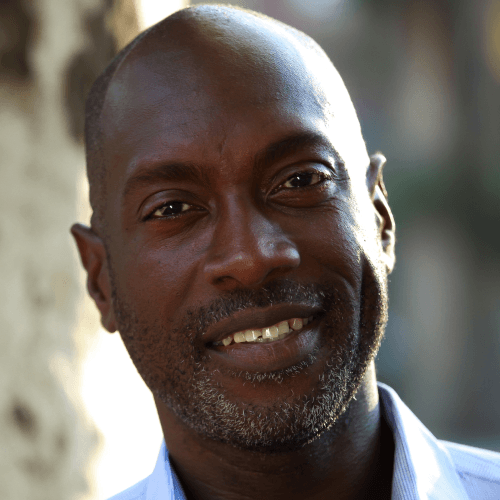 Paul is a tall, black, middle-aged man. He has a greying mustache and bald head.