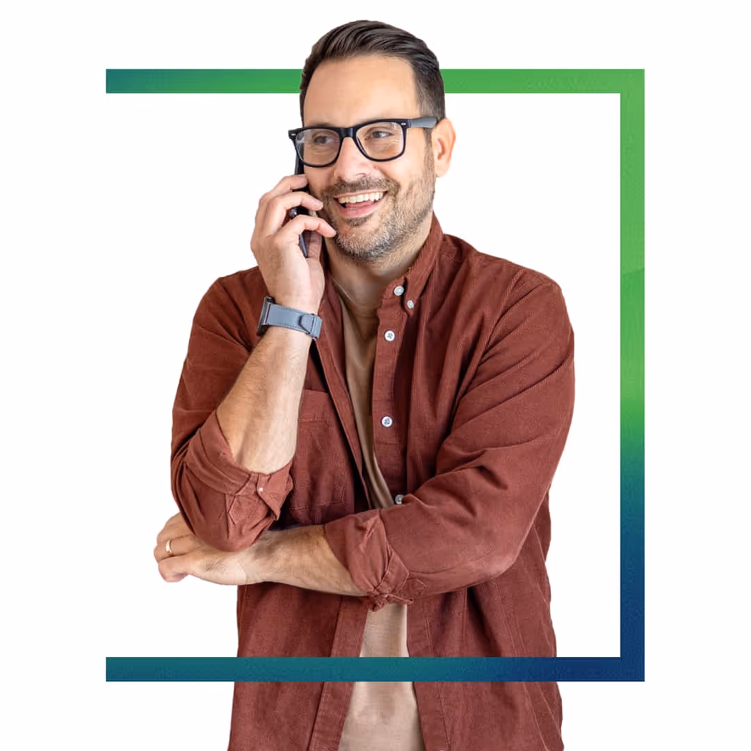Smiling man with glasses and beard talking on a smartphone, wearing a brown shirt and watch.