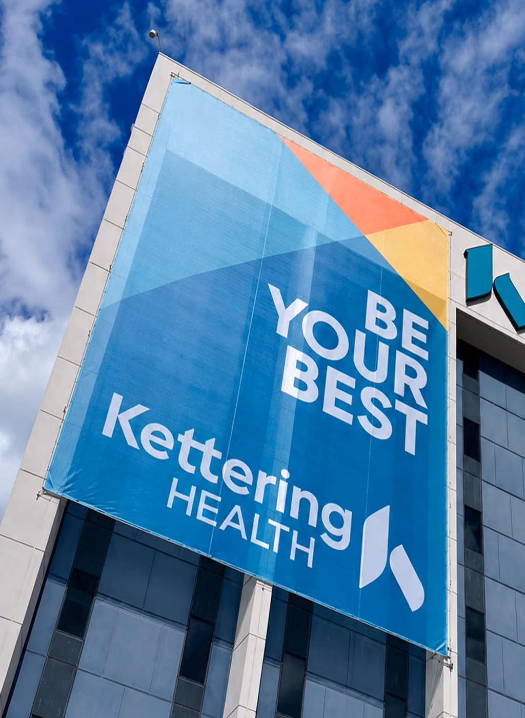 Large Kettering Health banner on building corner says Be Your Best with logo and colorful design.