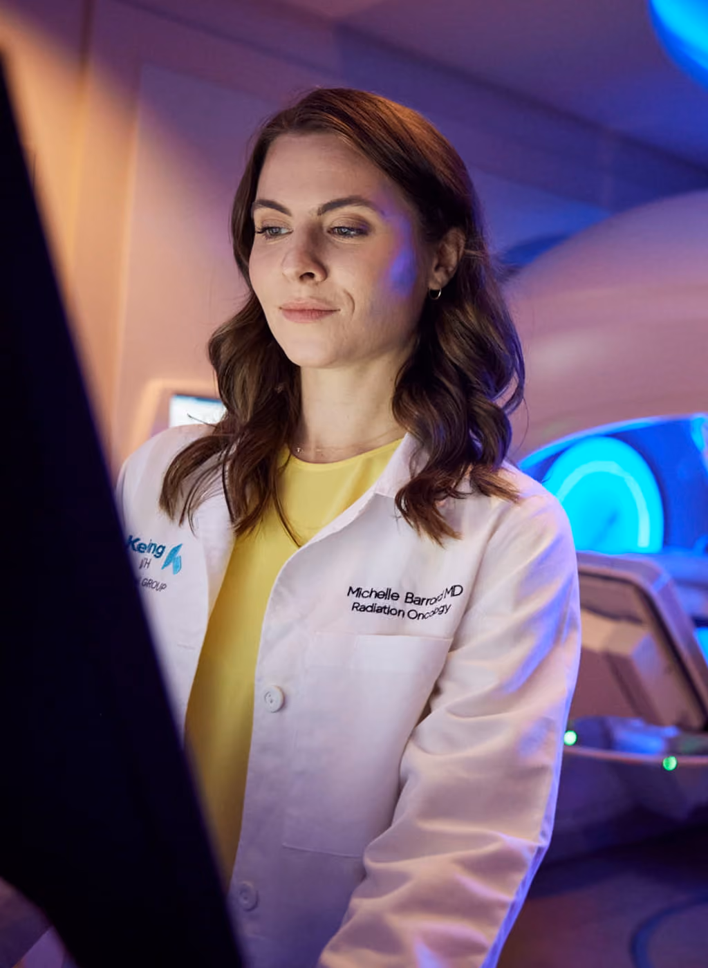 Female doctor in a white coat operating medical equipment in a clinical setting with blue lighting.