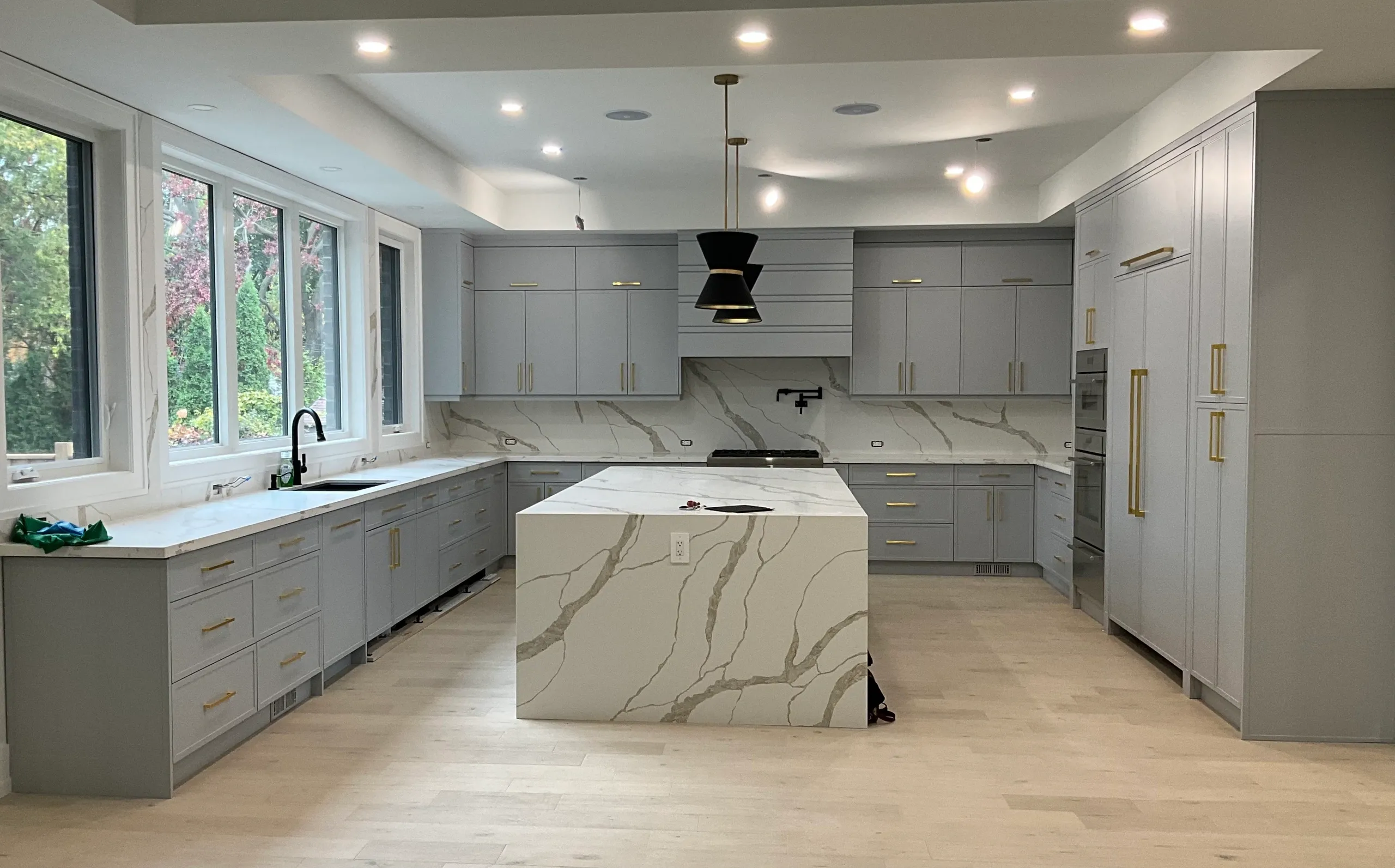 Modern kitchen with gray cabinetry, marble-patterned island and backsplash, large windows, and black pendant light fixture.