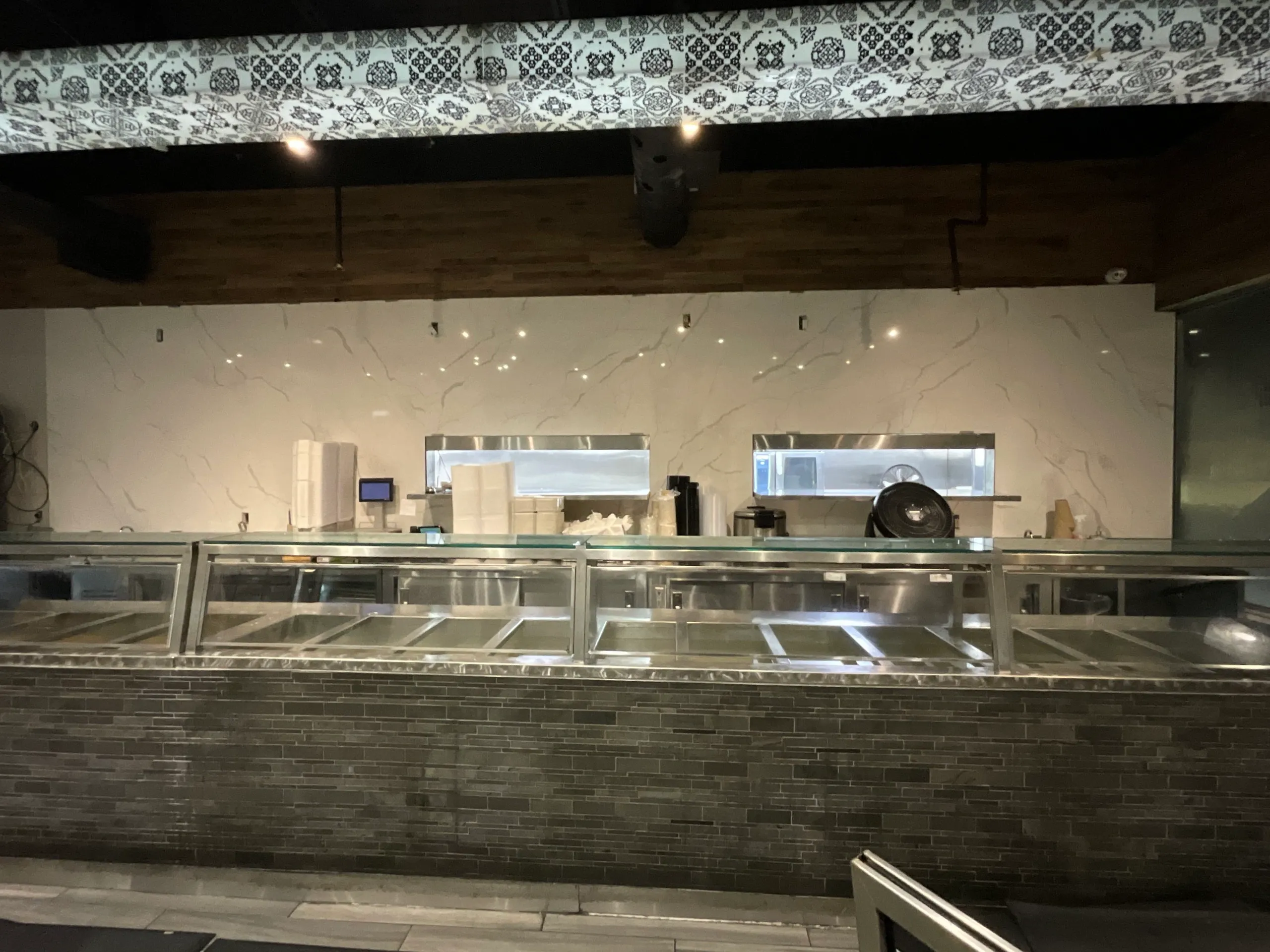 Empty commercial food service counter with glass sneeze guard and marble wall background.