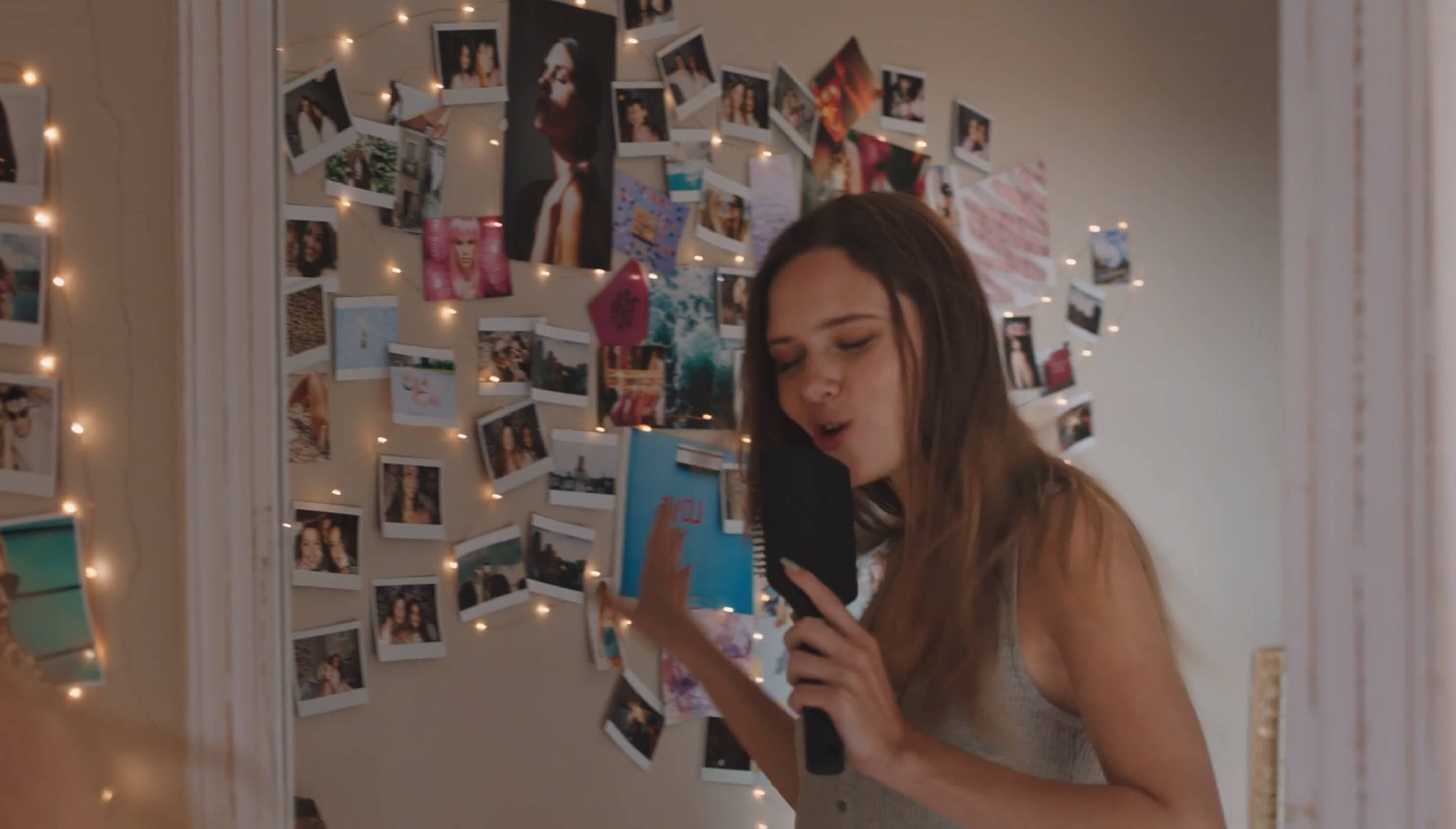 Caucasian teenage girl singing into a hairbrush in front of her bedroom wall covered in photos