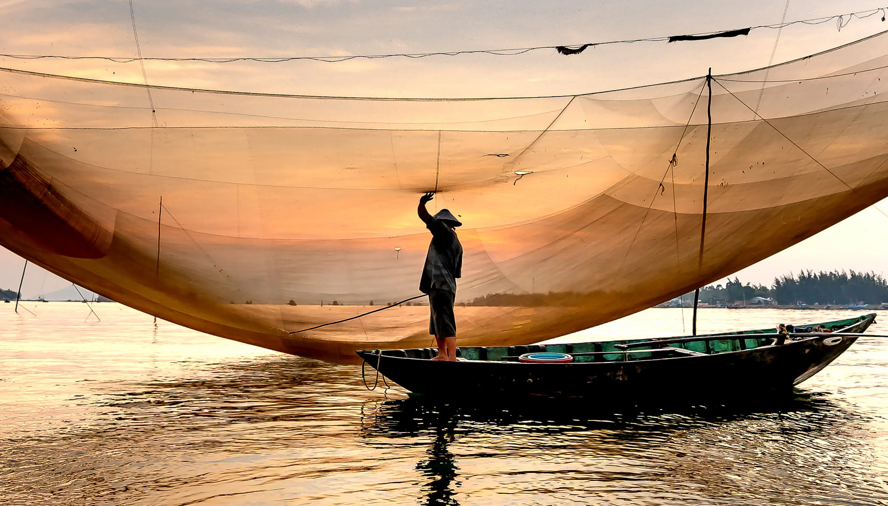 Silhouette of a man standing in a sailboat at sunset