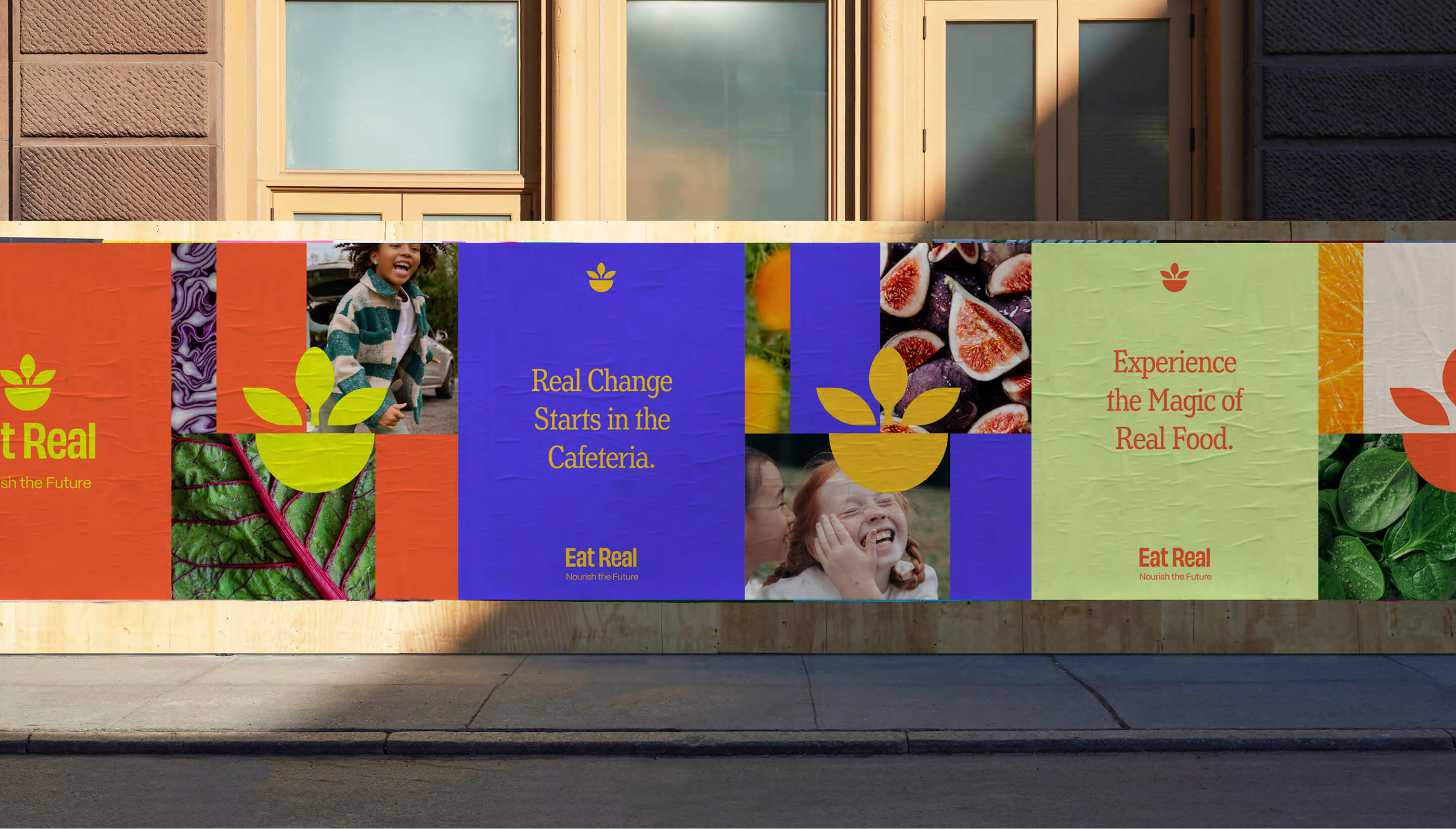 On an urban sidewalk, Eat Real posters are pasted onto a construction site wall. They are colorful, show images of healthy children having fun and real, fresh food.