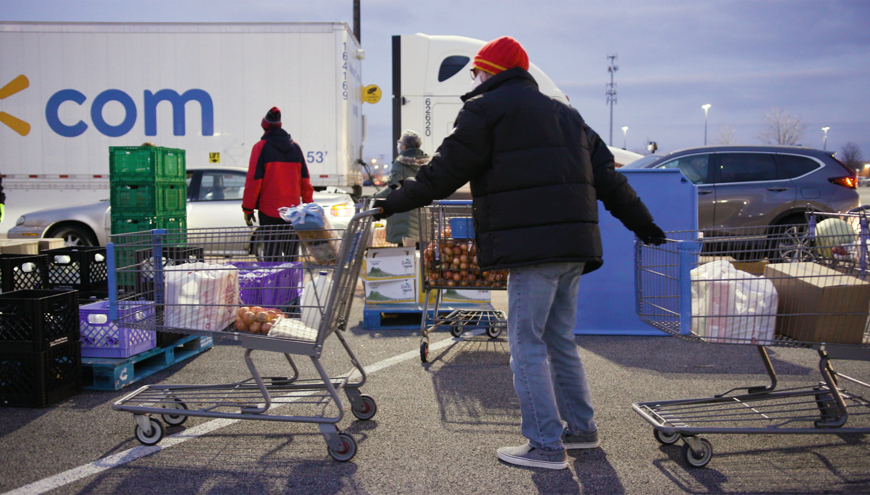 Man pulling two shopping carts full of food through a parking lot at a food bank