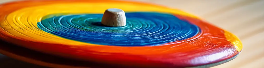 A spinning top with concentric layers of rainbow colors, featuring a wooden handle at the center, resting on a wooden surface.