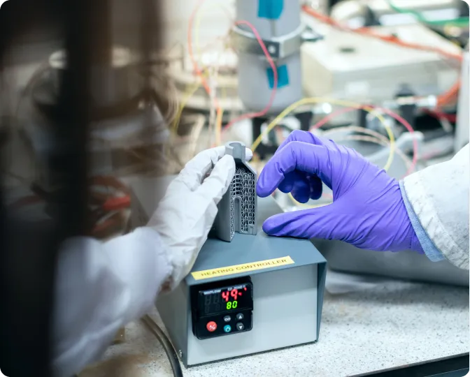 Engineer in gloves holding a prototype part next to a temperature controller