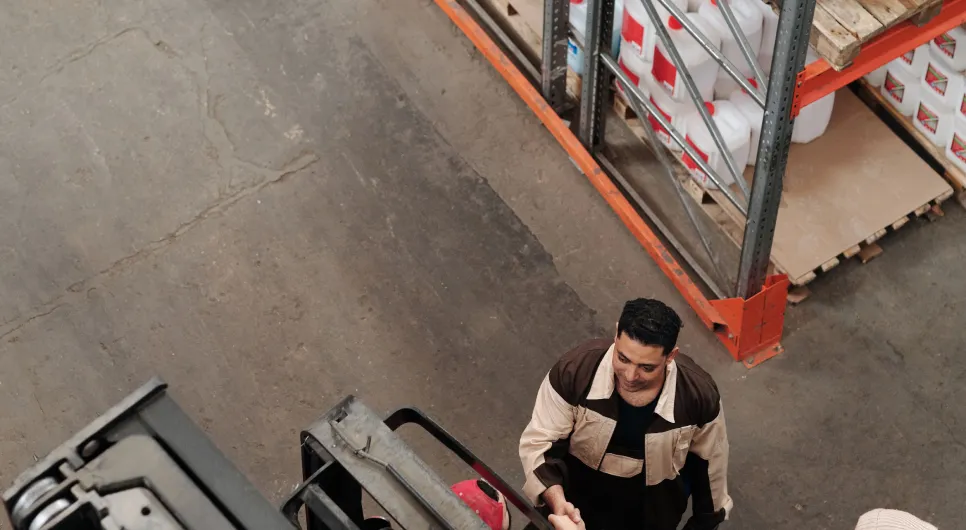 Warehouse worker beside a forklift and stocked shelving