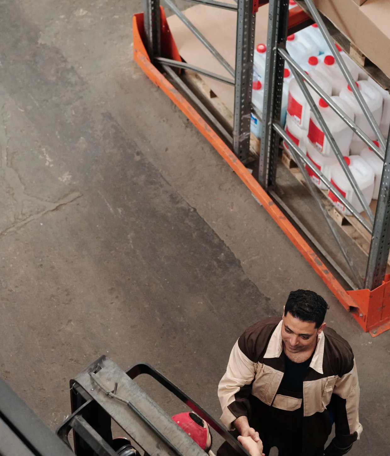 Warehouse worker beside a forklift and stocked shelving