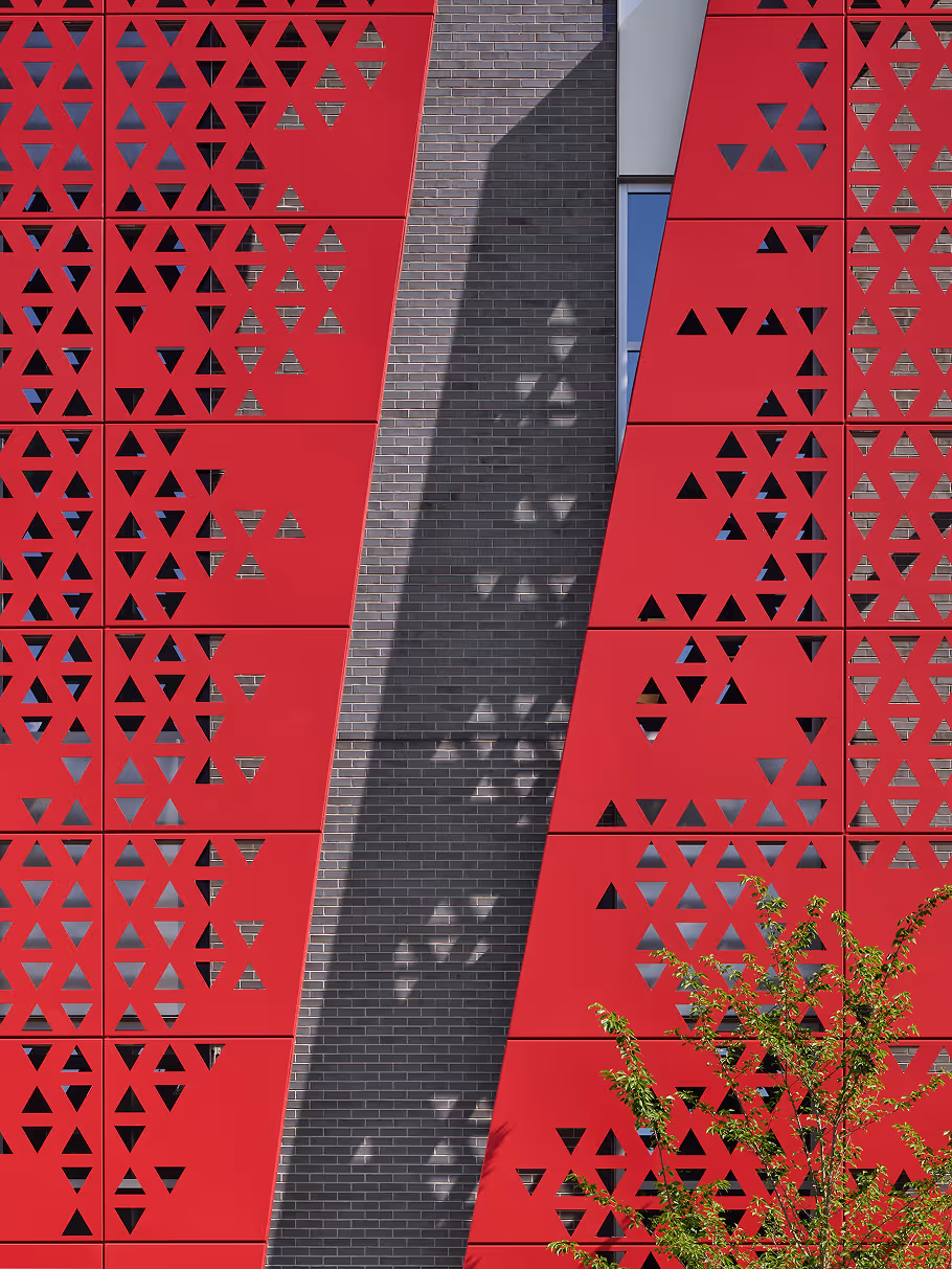 Architectural facade with red perforated metal panels.
