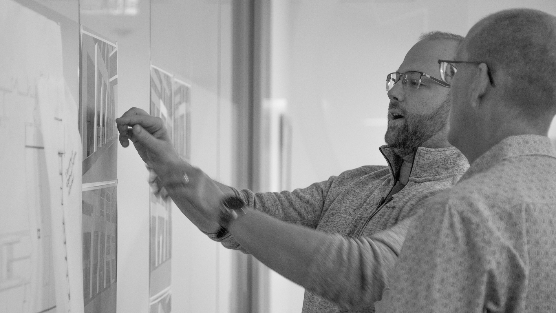 Two team members reviewing architectural plans on a wall.
