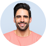 Smiling man with dark hair and beard wearing a coral pink shirt against a light blue background.