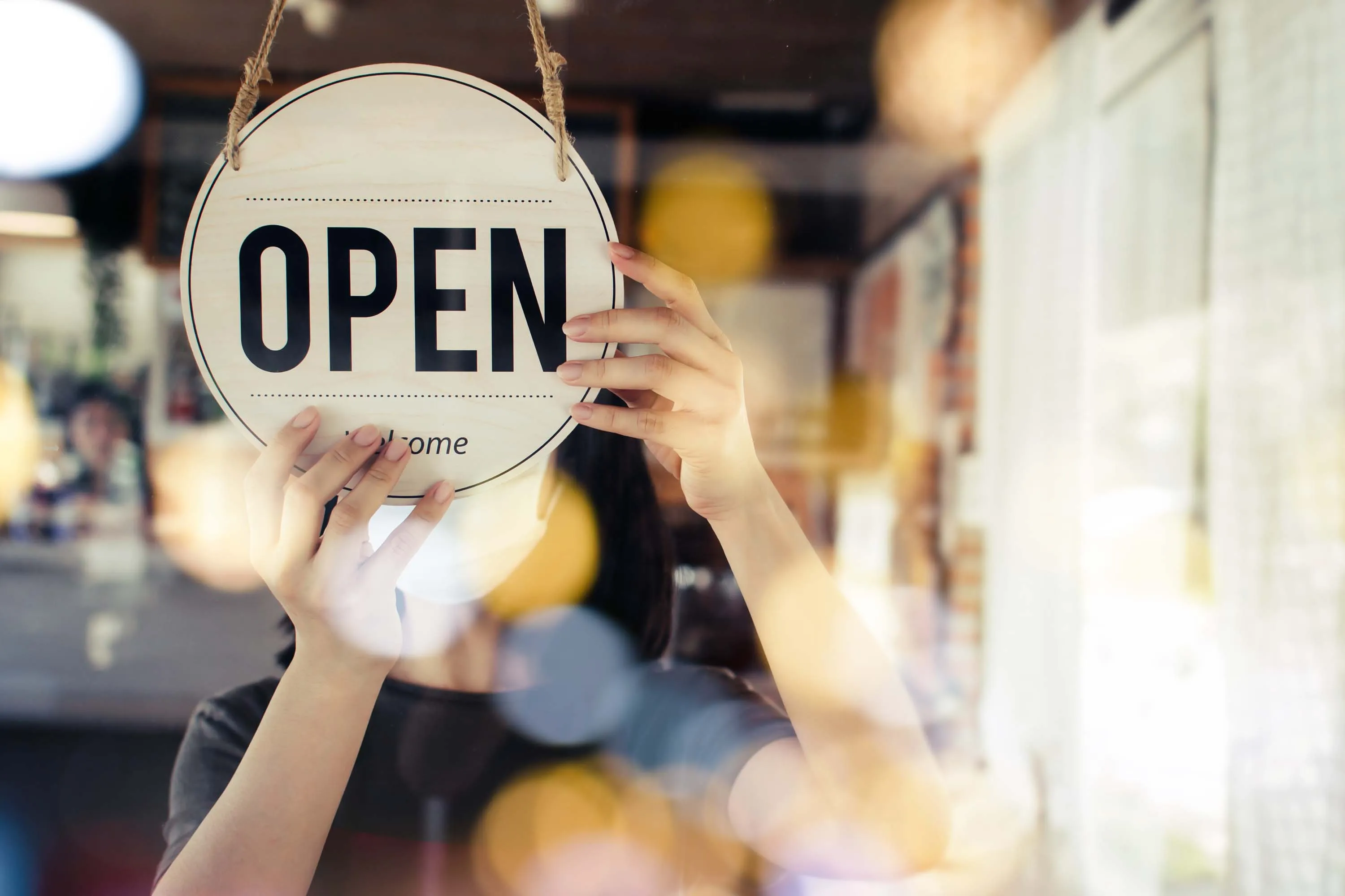 Person hanging an “OPEN” sign on the front door of a shop.