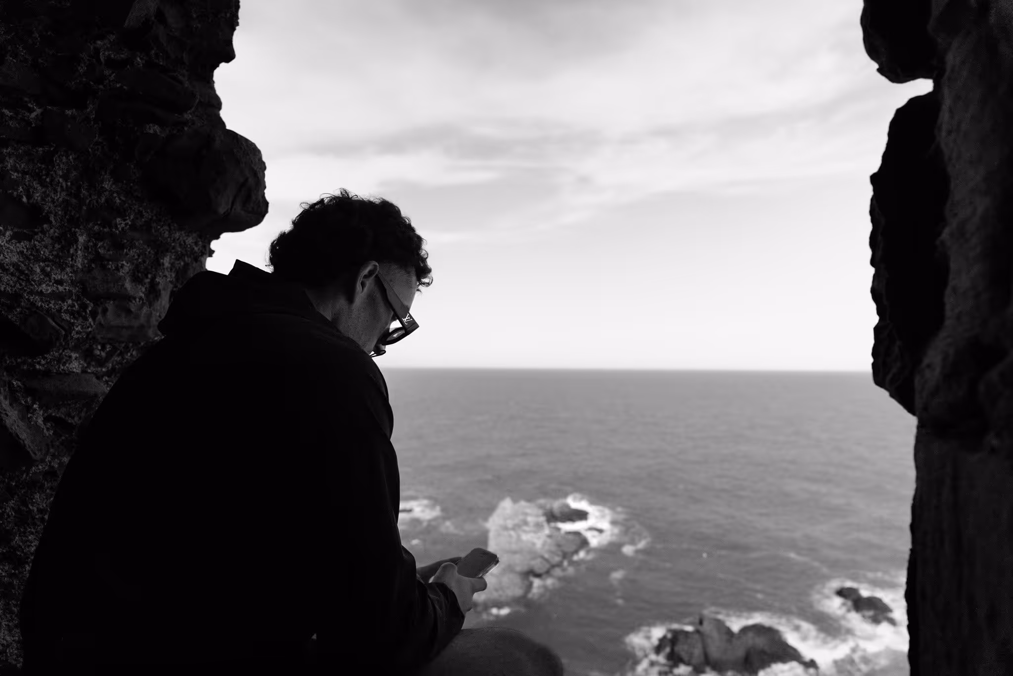 Photo ésthétique d'unb homme avec son téléphone sur le bord de la mer près de roché
