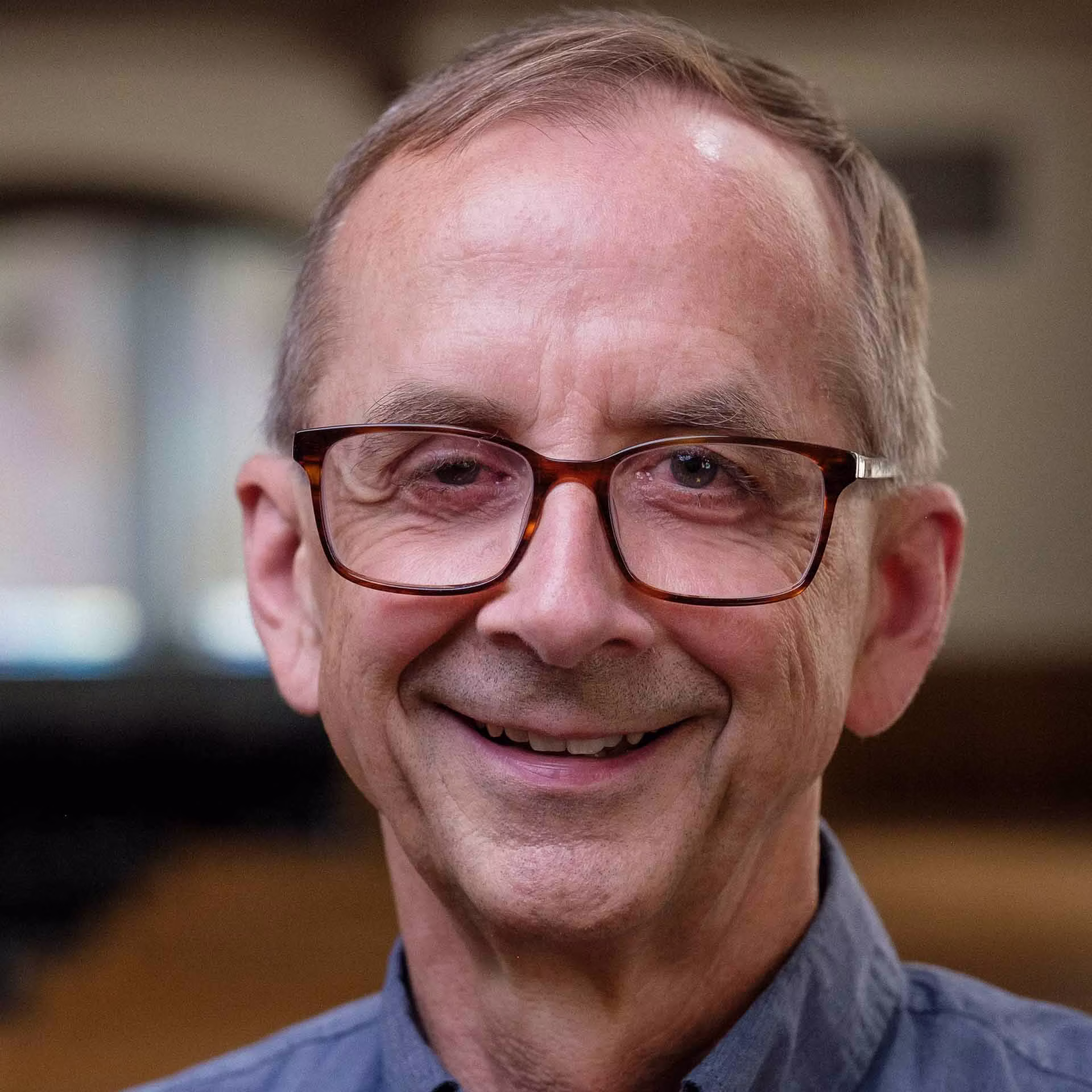 Older man with glasses smiling warmly in a blue shirt