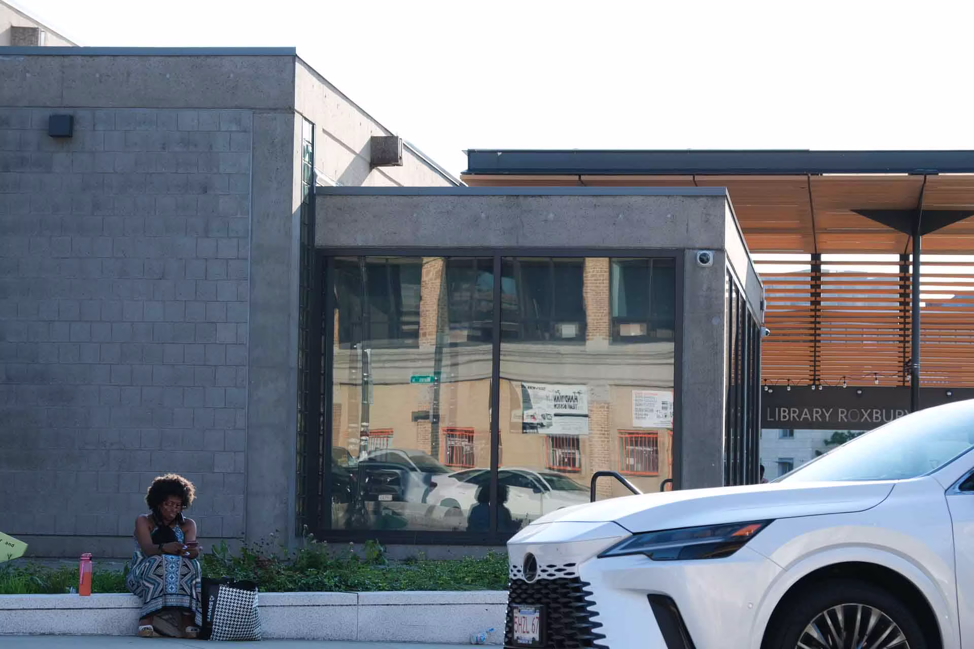 Person sitting outside Roxbury Library with white car and modern building