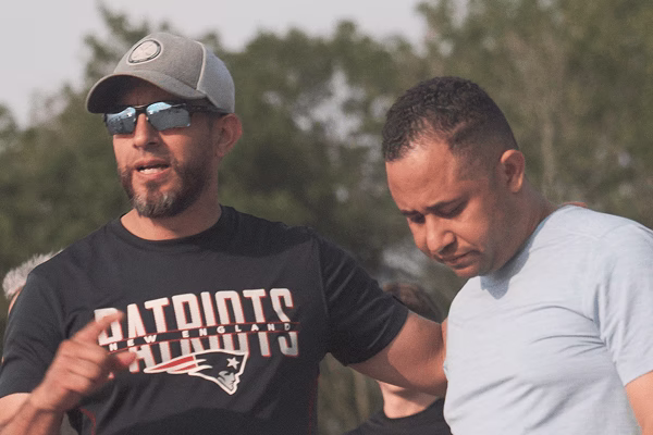 Two men outdoors, one wearing Patriots shirt and sunglasses