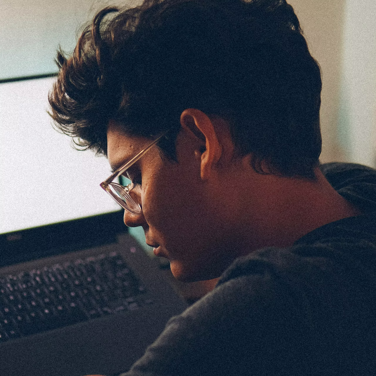 Person with glasses working intently on a laptop in low light